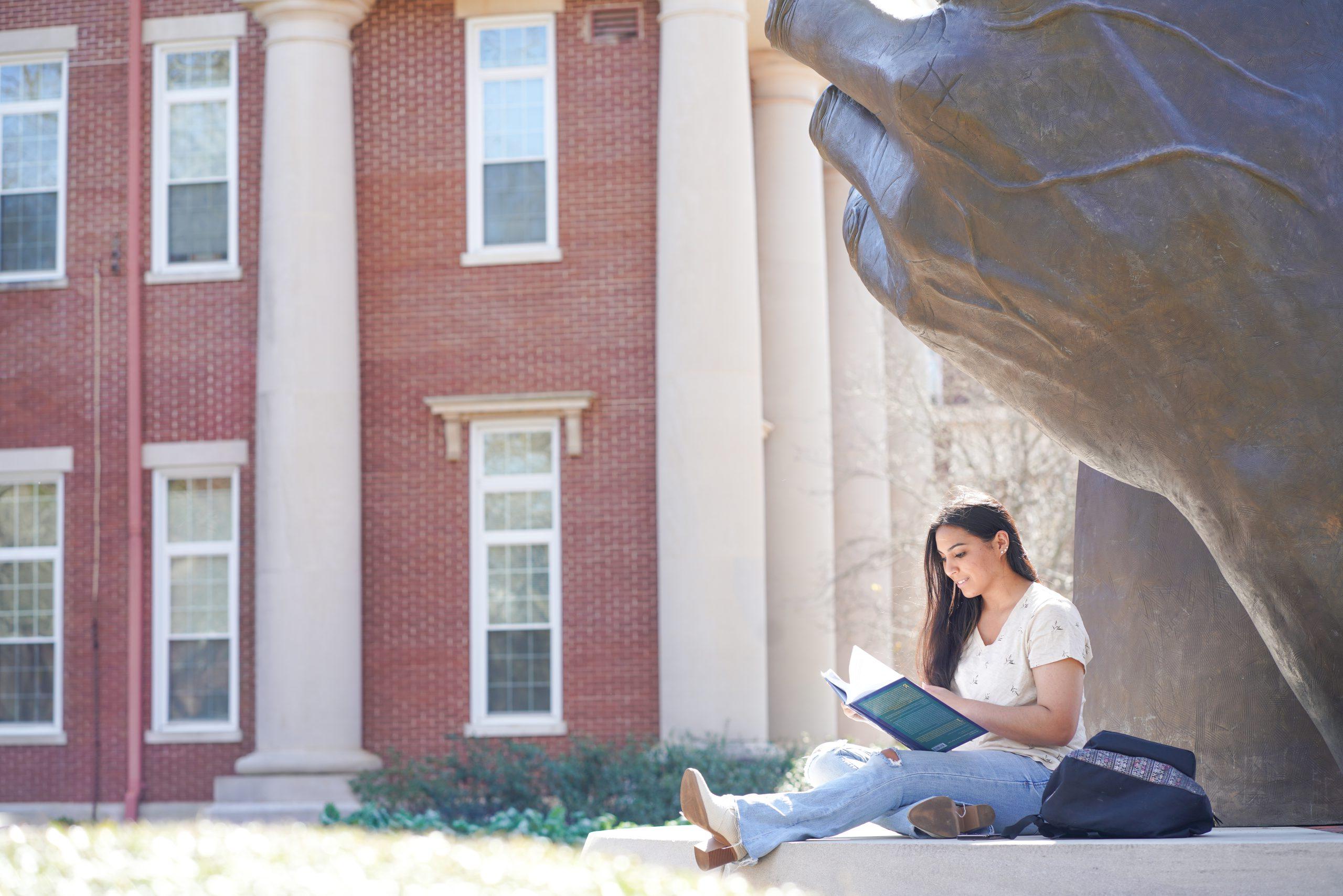 A University of Montevallo student studies underneath the Becoming statue.
